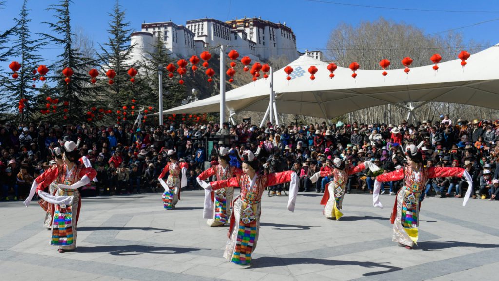 Traditional dance performance during the Tibetan New Year celebrations in Xizang, with the iconic Potala Palace in the background.