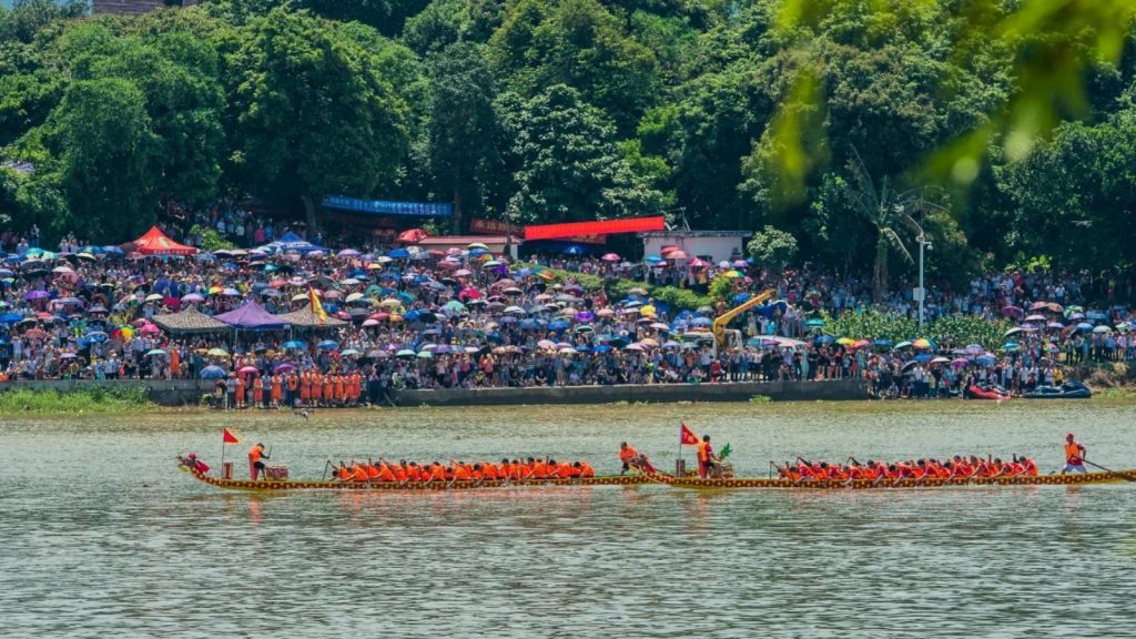 A traditional dragon boat race with teams on the river and spectators along the shore.
